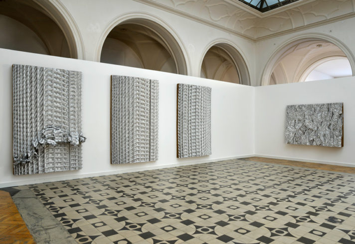 Ausstellungsansicht, Sollbruchstelle/Centerpoint, 2013/15 (Triptychon) 3 x Wellpappenrelief, mit Gesso bemalt, Bleistift, Permanentmarker 240 x 150 x 25 cm, Fahnen, 2013, Wellpappenrelief, mit Gesso bemalt, Bleistift, Permanentmarker 150 x 200 x 24 cm © VG Bild-Kunst, Bonn 2018/ Martin Spengler, Foto: Martin Spengler