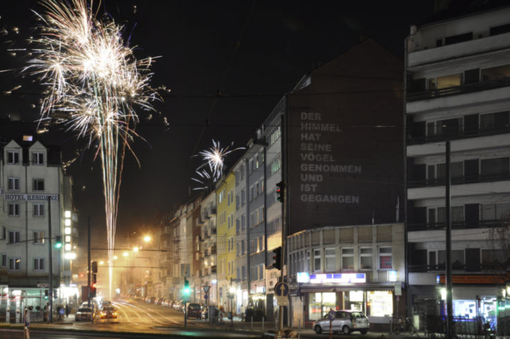 Gitti Göc, 2015, Worringer Platz, Düsseldorf, Pigment-Schrift auf Fassade, ca. 7,60 m x 6 m Installationssicht am Silvesterabend 2015/2016. Ein türkischer Vers von Ilhan Berk in der Übersetzung des Lyrikers Achim Wagner auf einer Fassade. Die Buchstaben bestehen nur aus aufgetupftem Pigment. Wind und Wetter werden die Schriftzeichen abwaschen und wegwehen.